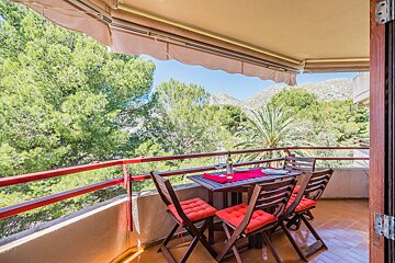 A balcony with a table and chairs and mountains in the background
