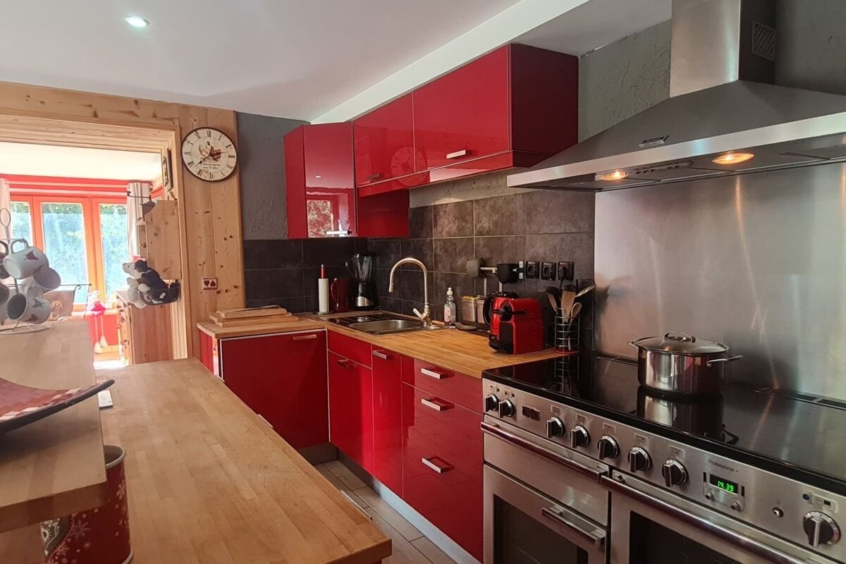 Modern kitchen featuring glossy red cabinets, wooden countertops, stainless steel appliances, and a dark tiled backsplash.