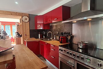 Modern kitchen featuring glossy red cabinets, wooden countertops, stainless steel appliances, and a dark tiled backsplash.
