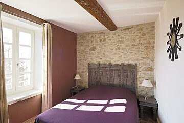 A bedroom with a stone wall and a purple bed