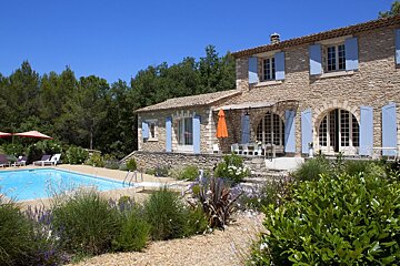 A large stone house with blue shutters and a swimming pool