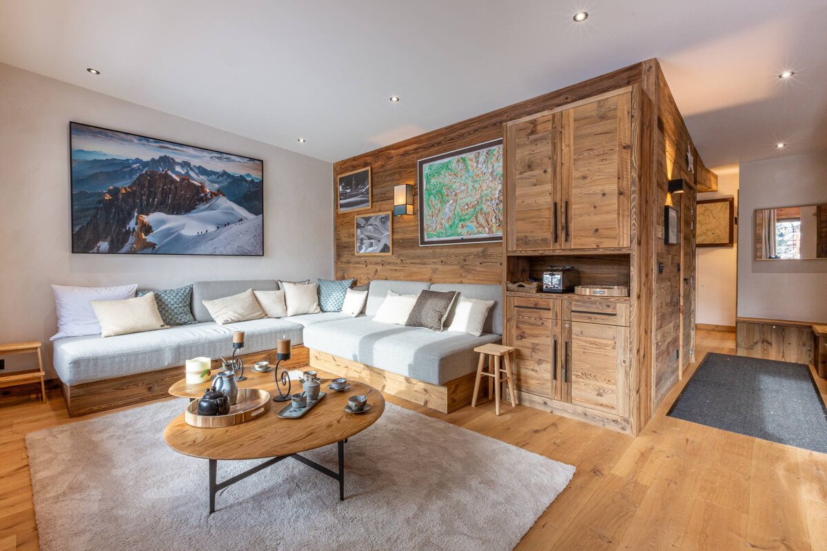 Cozy chalet living room with rustic wooden decor, a large L-shaped sofa, mountain artwork, and a coffee table with a tea set.