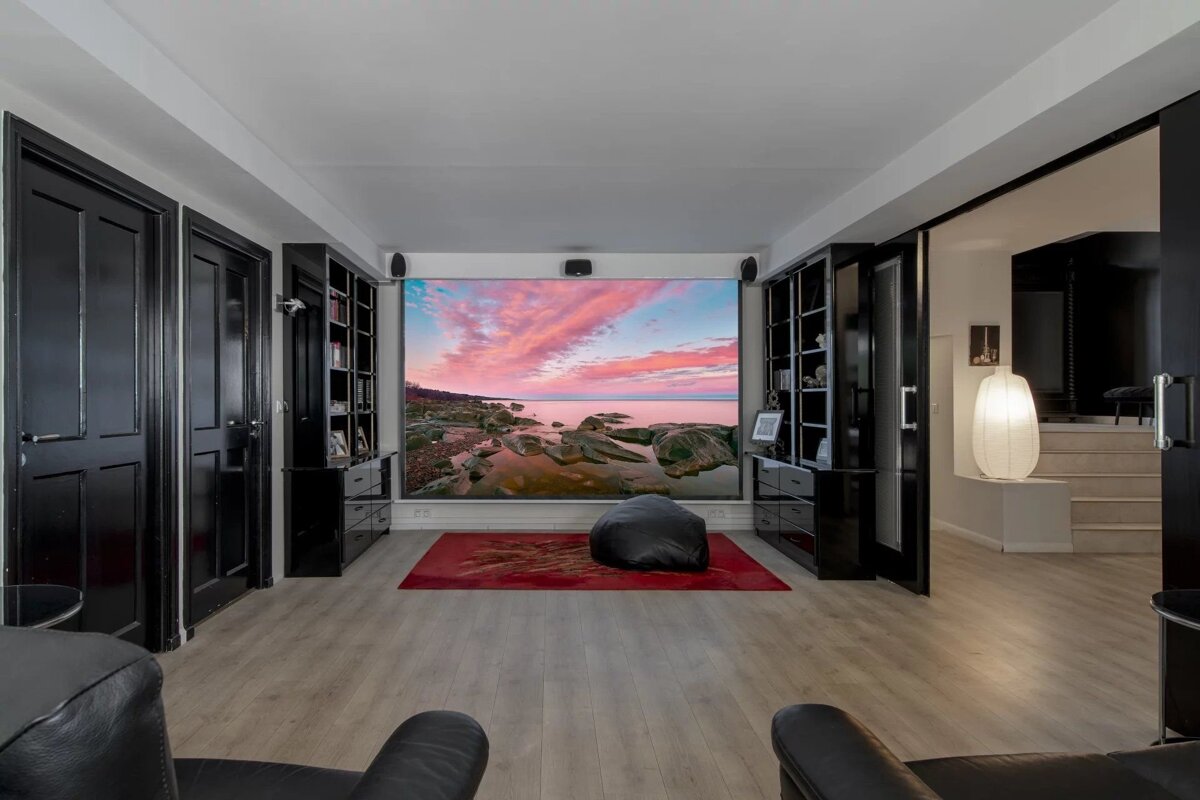 Modern home theater room featuring black cabinetry and a large projection screen displaying a vibrant coastal sunset.