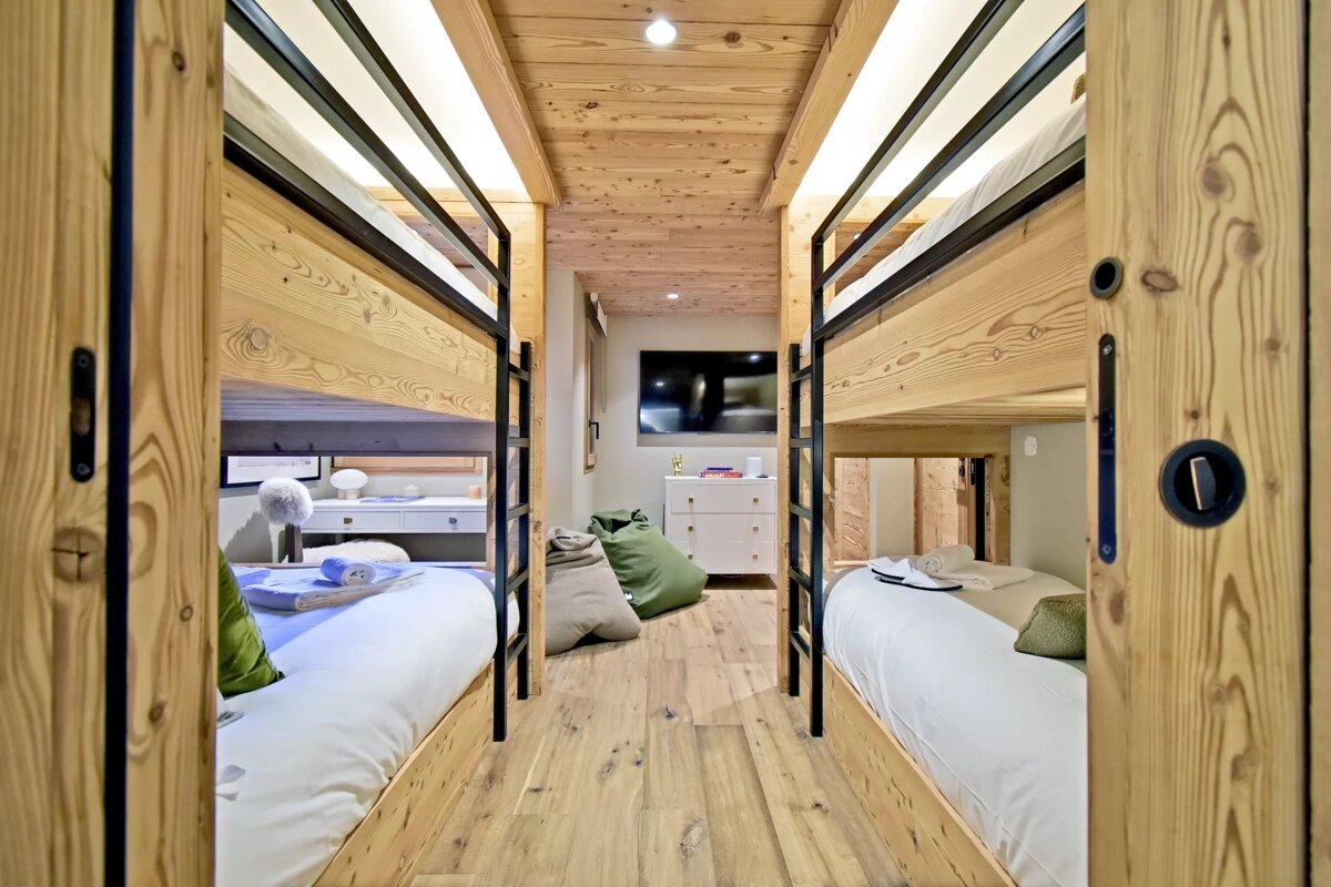 Cozy wooden cabin bedroom featuring built-in bunk beds on both sides, looking down a hallway toward a TV and bean bag chairs.