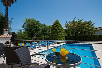 Two glasses of orange juice sit on a table in front of a swimming pool