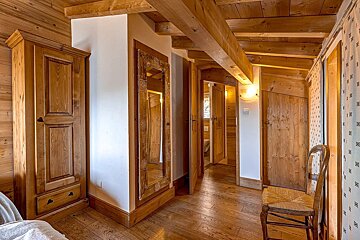 A cozy, rustic room or hallway with extensive light wood paneling, exposed beams, multiple doors, a wardrobe, a decorative mirror, and a chair.