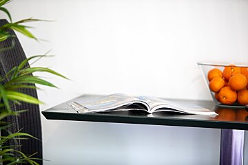 An open magazine sits on a table next to a bowl of oranges