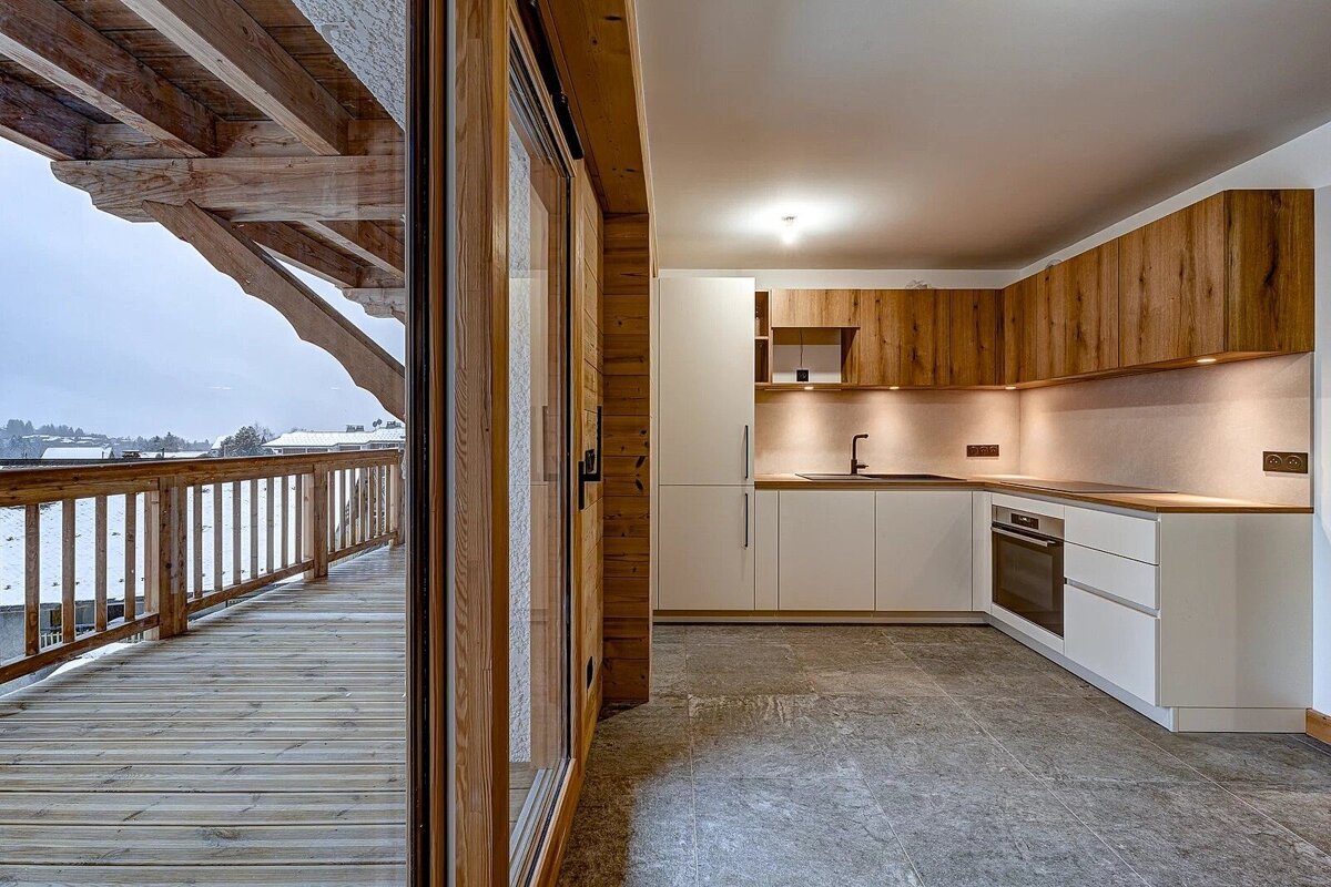 Stylish kitchen with wood and white cabinetry, seamlessly connected to a wooden balcony offering a serene snowy vista.