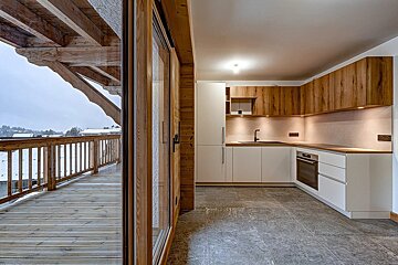 Modern chalet kitchen with white and wood cabinets, next to a wooden balcony overlooking a snowy winter landscape.