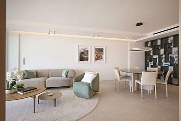 A bright, modern open-plan living and dining room with a neutral sofa, green armchair, coffee tables, dining set, and decorative wall shelving.