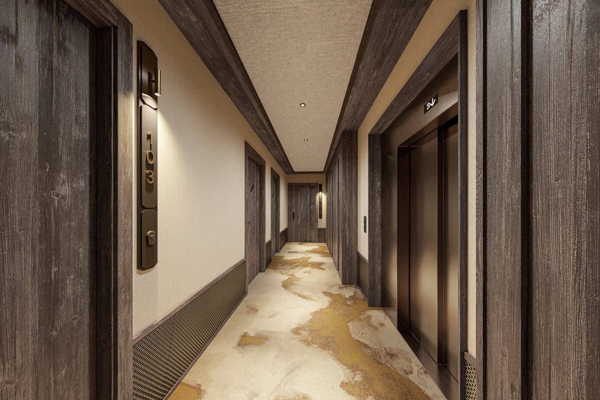 A modern hotel hallway featuring dark wood paneling, elegant wall lighting, an elevator, and a unique textured gold-patterned floor.
