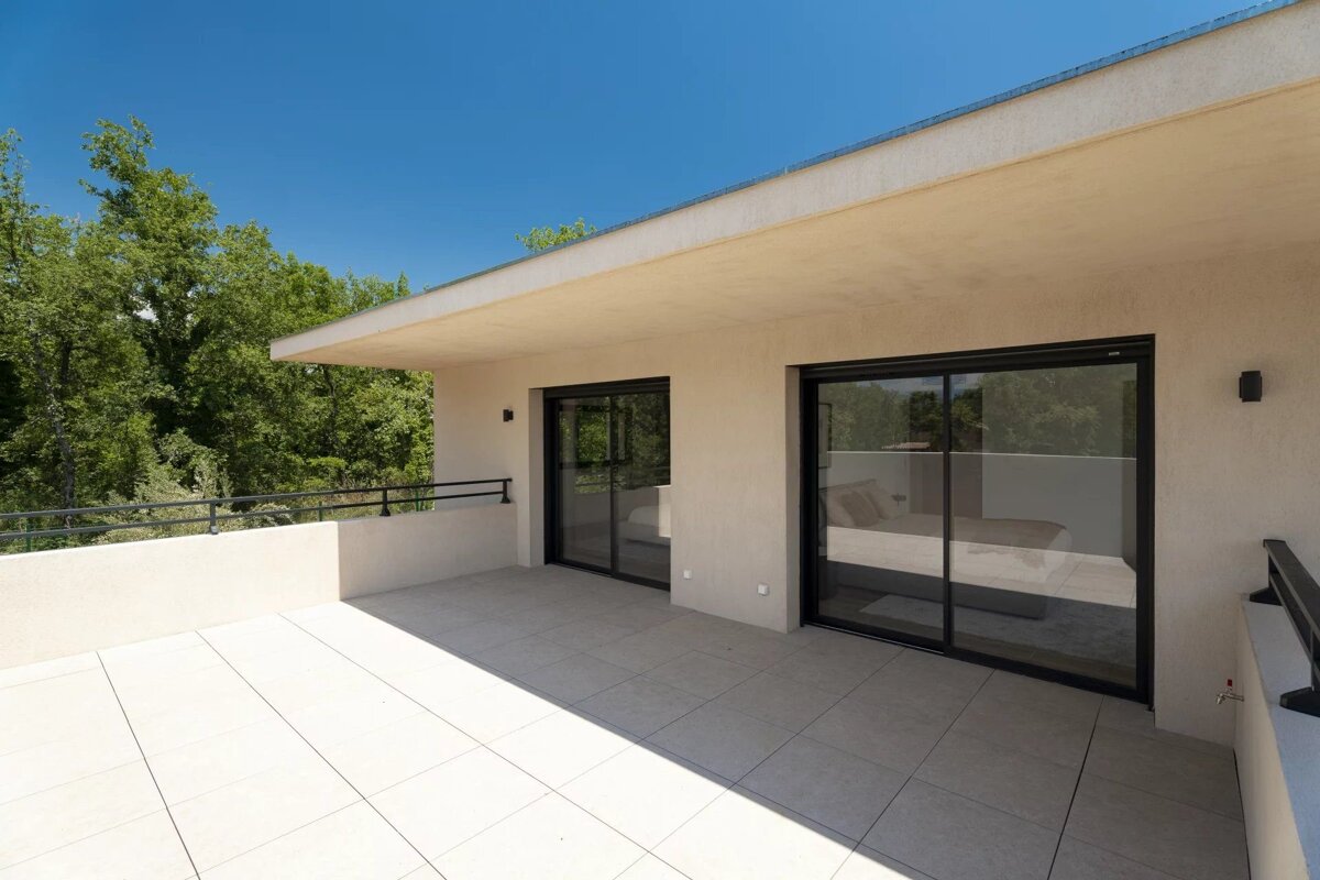 Modern tiled balcony with sliding glass doors opening to a scenic view of green trees under a bright blue sky.