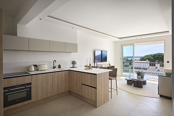 Modern open-plan apartment featuring a light wood kitchen, cozy living area, and sliding doors opening to a scenic balcony view.