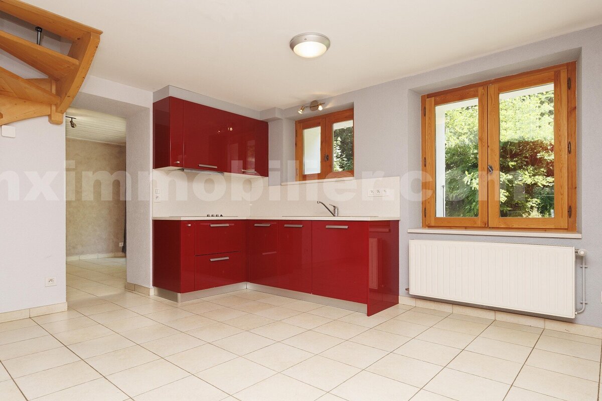 Bright modern kitchen with glossy red cabinets, light tiled floor, and wooden-framed windows. A staircase is visible on the left.