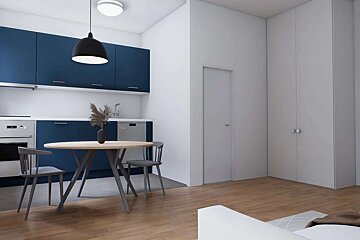 Minimalist studio with a modern blue kitchen, round dining table, white walls, and built-in storage, all on a warm wooden floor.