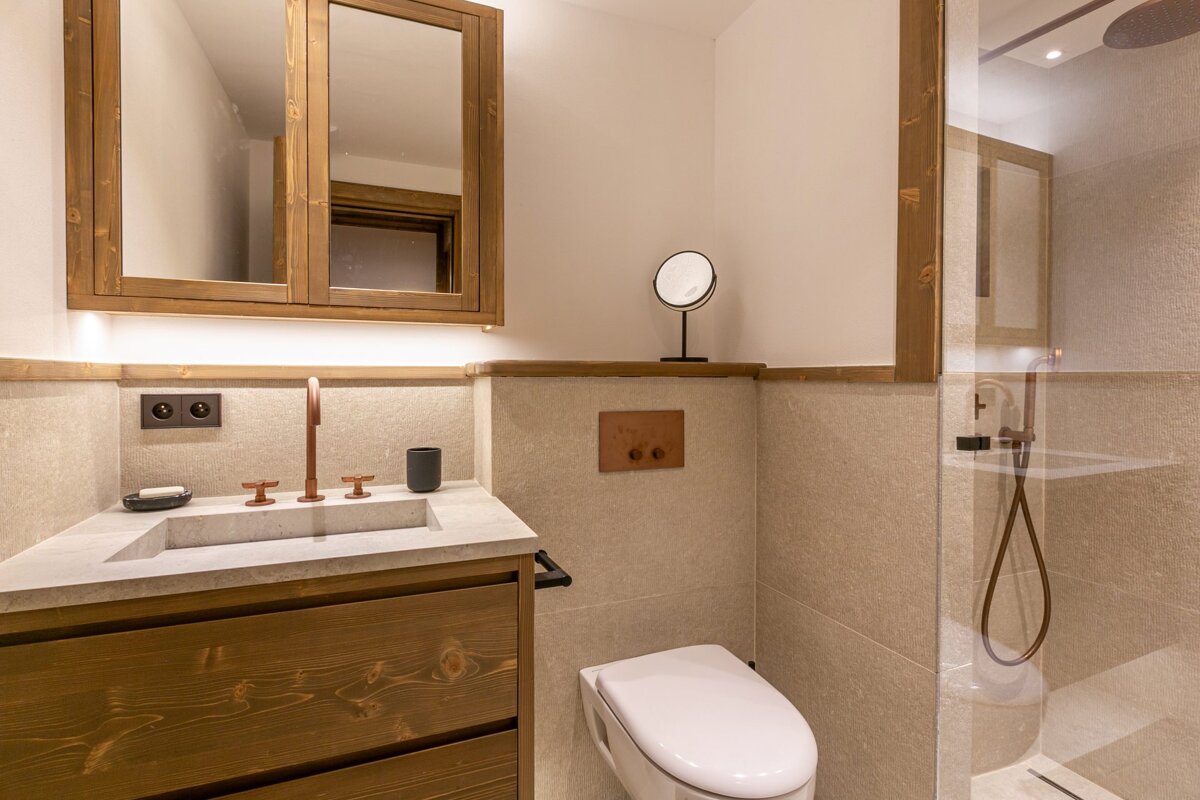 Stylish modern bathroom featuring wooden cabinetry, a concrete vanity with copper fixtures, a toilet, and a glass-enclosed shower.