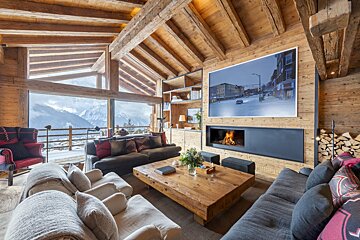 Luxurious rustic chalet living room with a stunning mountain view, cozy fireplace, large sofas, and exposed wooden beams throughout.