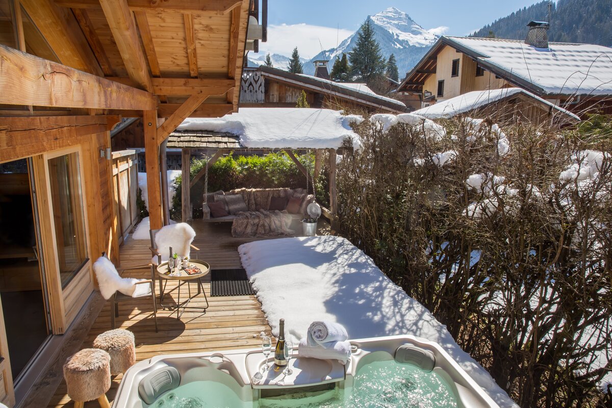 A hot tub on a snowy deck with a mountain in the background
