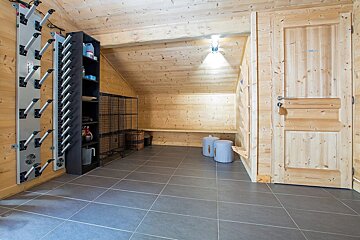 A rustic wooden ski room with boot dryers, storage shelves, benches, a tiled floor, and a wooden door, illuminated by a ceiling light.