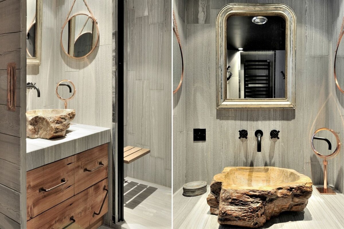 Chic rustic bathroom featuring a raw stone sink, wood vanity, textured gray walls, and stylish gold and copper mirrors.