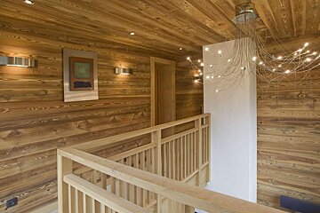 A cozy, modern interior features extensive wood paneling on walls/ceiling, a wooden staircase railing, and a unique chandelier with numerous small lights.