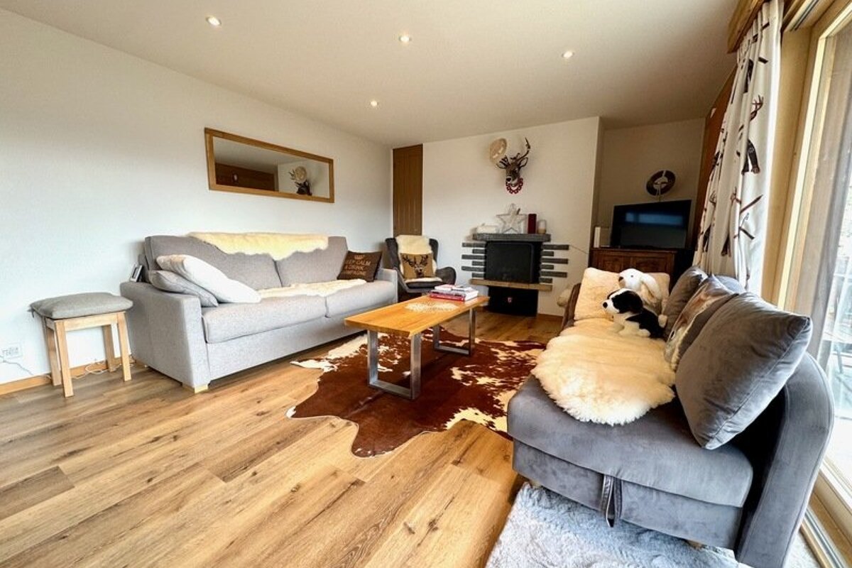 Cozy chalet-style living room with grey sofas, a wooden coffee table, a cowhide rug, and a fireplace with a deer head mount.