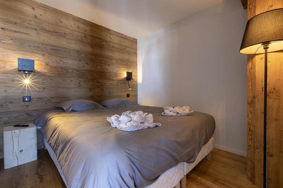 A cozy bedroom featuring a rustic wooden accent wall, a bed with gray linen, warm wall sconces, and a floor lamp creating an inviting ambiance.