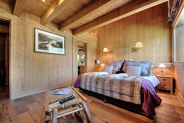 A cozy, wood-paneled bedroom with a large bed, furry blanket, and mountain-themed decor, exuding a warm chalet ambiance.