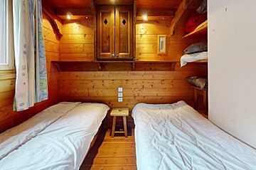 A wooden bedroom with two beds and a stool