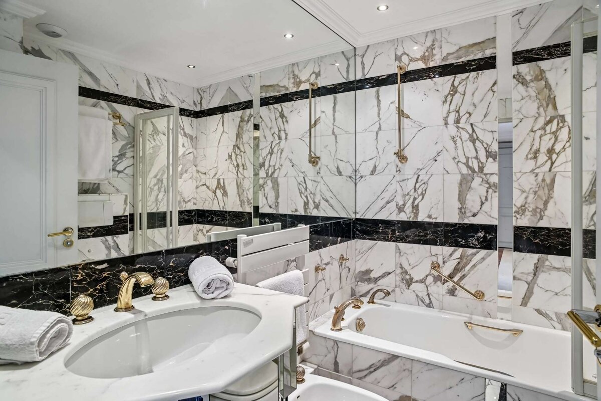 Luxurious bathroom boasts white and black marble walls, gold fixtures, a large mirror, sink, and bathtub.