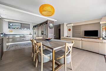 Modern open-plan apartment with dining table, kitchen, and living area, featuring a vibrant orange pendant light.