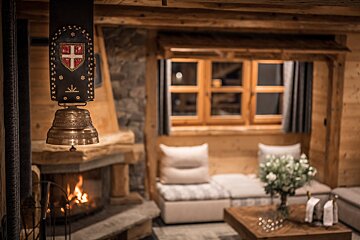 Cozy alpine chalet interior with a burning fireplace, wooden furniture, and a decorative cowbell hanging in the foreground.