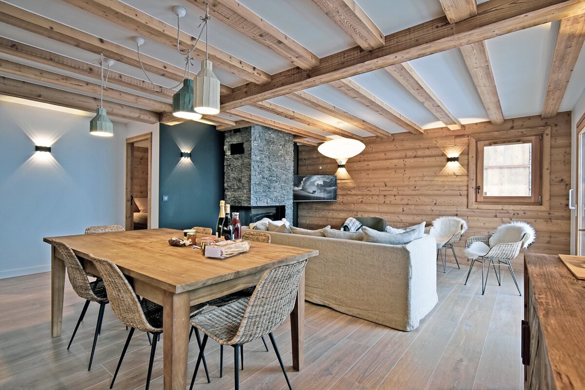 Modern rustic cabin interior featuring a wooden dining set, exposed ceiling beams, a stone fireplace, and a cozy living area.