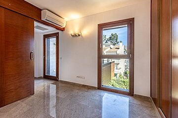 An empty room with polished marble floors, a wooden sliding door, and a tall wood-framed window overlooking a sunny outdoor view.
