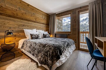 A bedroom with a bed and a desk with a view of the mountains