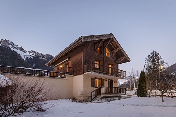 A house with snow on the ground and mountains in the background