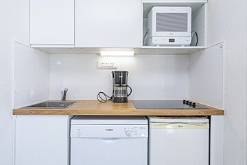 Compact white kitchen with wooden counter, sink, stovetop, coffee maker, microwave, dishwasher, and mini-fridge.