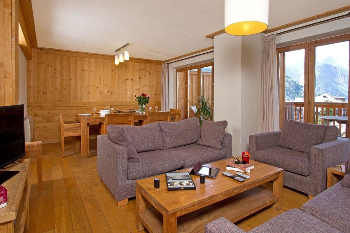 Cozy alpine chalet living room with grey sofas, a wooden coffee table, and glass doors looking out to scenic mountains.