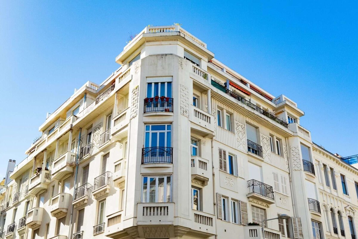 An ornate white corner building with many windows and balconies stands against a clear blue sky.