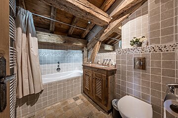 Cozy, rustic attic bathroom with exposed wooden beams, tiled walls, a bathtub with curtain, wooden vanity, and toilet.