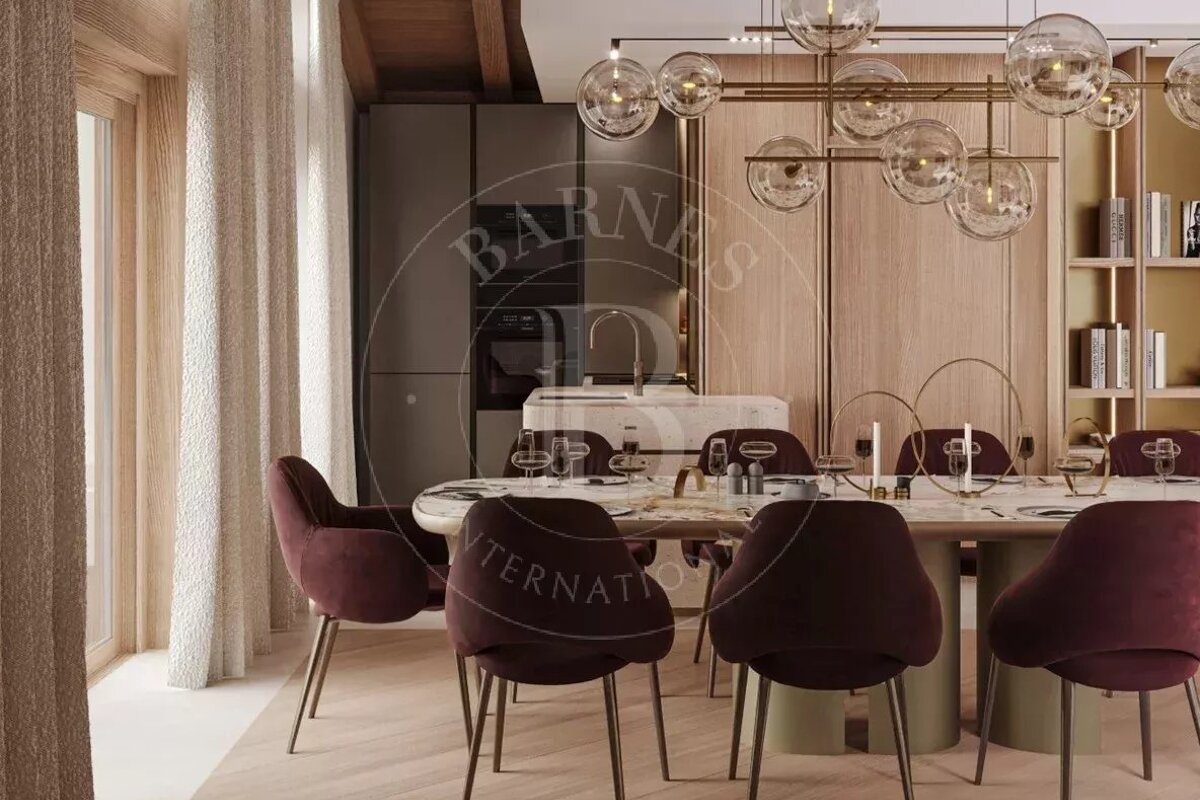 An elegant dining room with a marble table, plush burgundy chairs, and a modern glass sphere chandelier, open to a chic kitchen area.