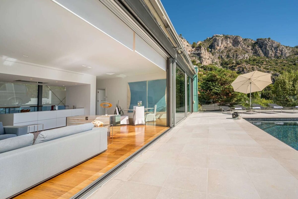 Chic interior with sliding glass doors opening to a pool patio and majestic mountains under a clear blue sky, blending modern luxury with nature.