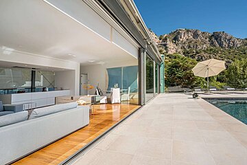 Chic interior with sliding glass doors opening to a pool patio and majestic mountains under a clear blue sky, blending modern luxury with nature.