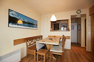 A cozy dining area with wooden furniture, including a table with a tablecloth and banquette seating. A panoramic mountain artwork adorns the wall.