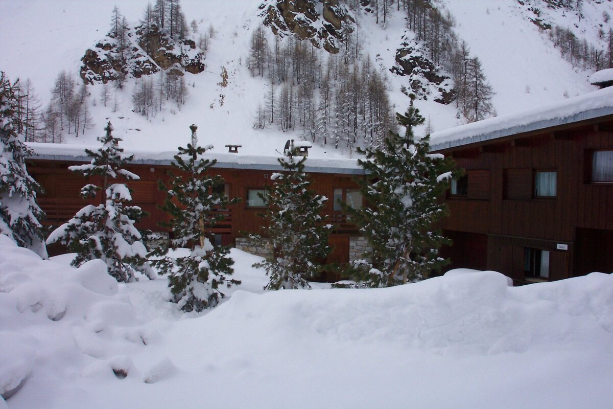 Snow-covered wooden chalets and pine trees are nestled in a snowy mountain landscape after heavy snowfall.