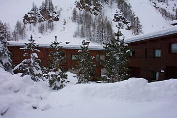 Snow-covered wooden chalets and pine trees are nestled in a snowy mountain landscape after heavy snowfall.
