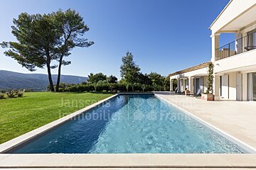 A large swimming pool in front of a large house with the word janssens immobilier on the bottom