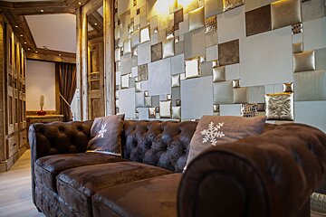 A luxurious chalet interior features a tufted brown sofa with snowflake pillows, facing a modern geometric wall of metallic and padded squares, framed by rustic wood.