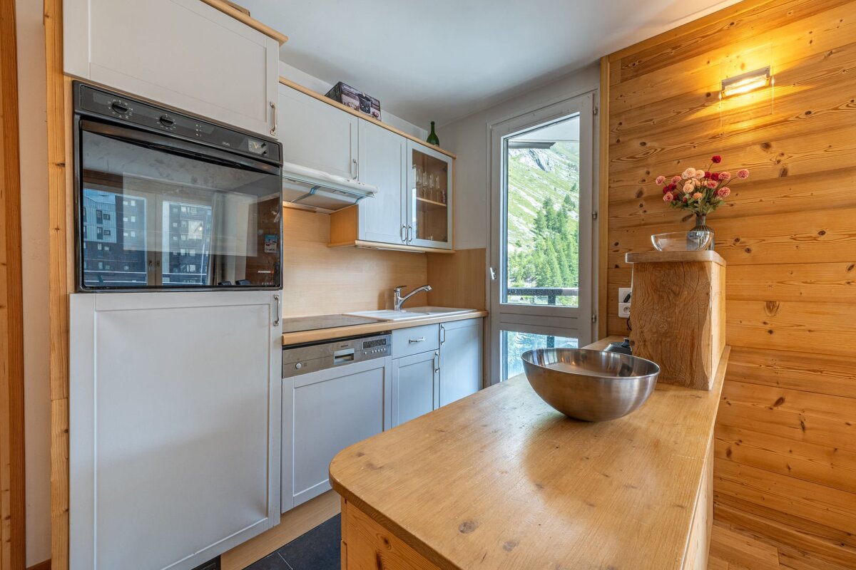 Modern kitchen with light cabinets, wood paneling, an oven, and a scenic mountain view through a large window.