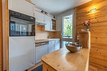 Modern kitchen with light cabinets, wood paneling, an oven, and a scenic mountain view through a large window.